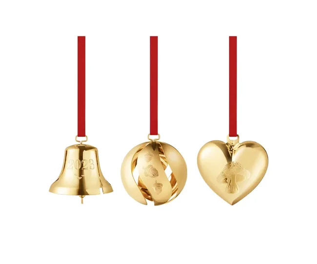 Gold Christmas ornaments: bell with "2023," spiral with acorns, and heart with a mushroom, all on red ribbons.