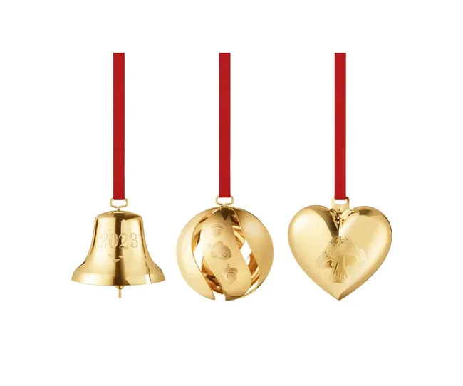 Gold Christmas ornaments: bell with "2023," spiral with acorns, and heart with a mushroom, all on red ribbons.