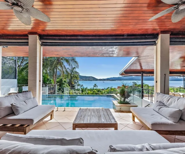Luxury villa patio with cushioned seating, overlooking an infinity pool and ocean view through glass railing.