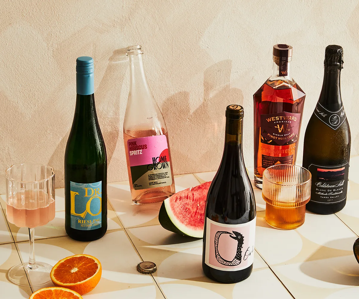 best summer drinks guide. photo of a pale backdrop and a line-up of bottles, glasses and cans showcasing beverage picks