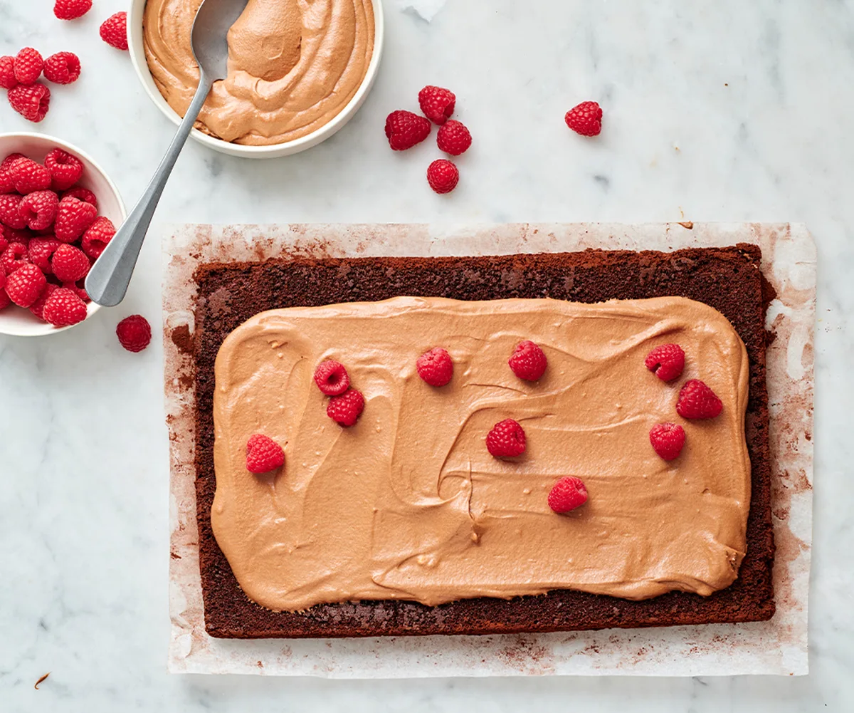 chocolate yule log sponge with light brown chocolate cream on top, scattered with raspberries