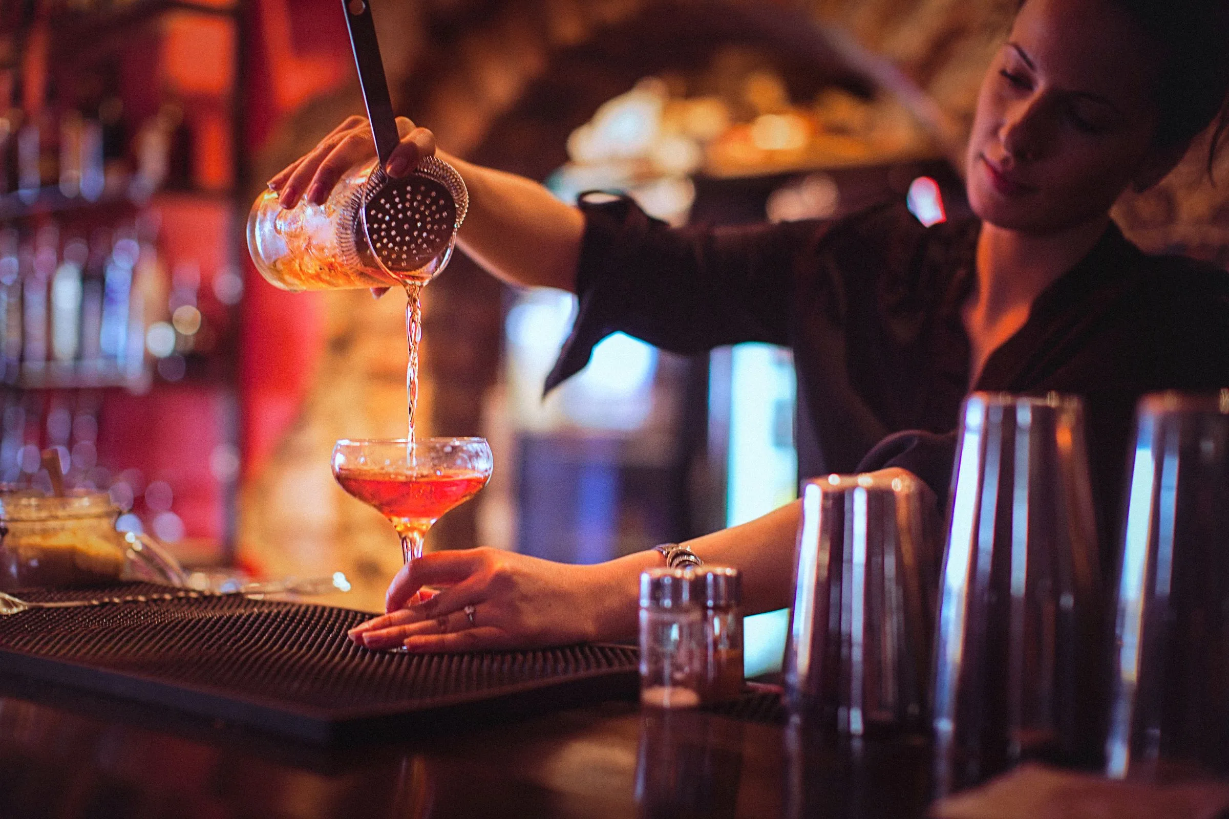 female bartender pouring a cocktail at a bar