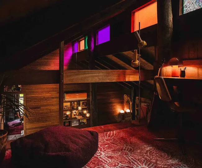 Cozy attic space with colorful stained glass windows, a desk, warm lighting, and a patterned rug.