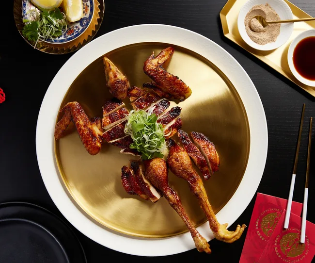 Roast chicken pieces arranged on a large gold and white plate, garnished with green herbs, surrounded by sauces.