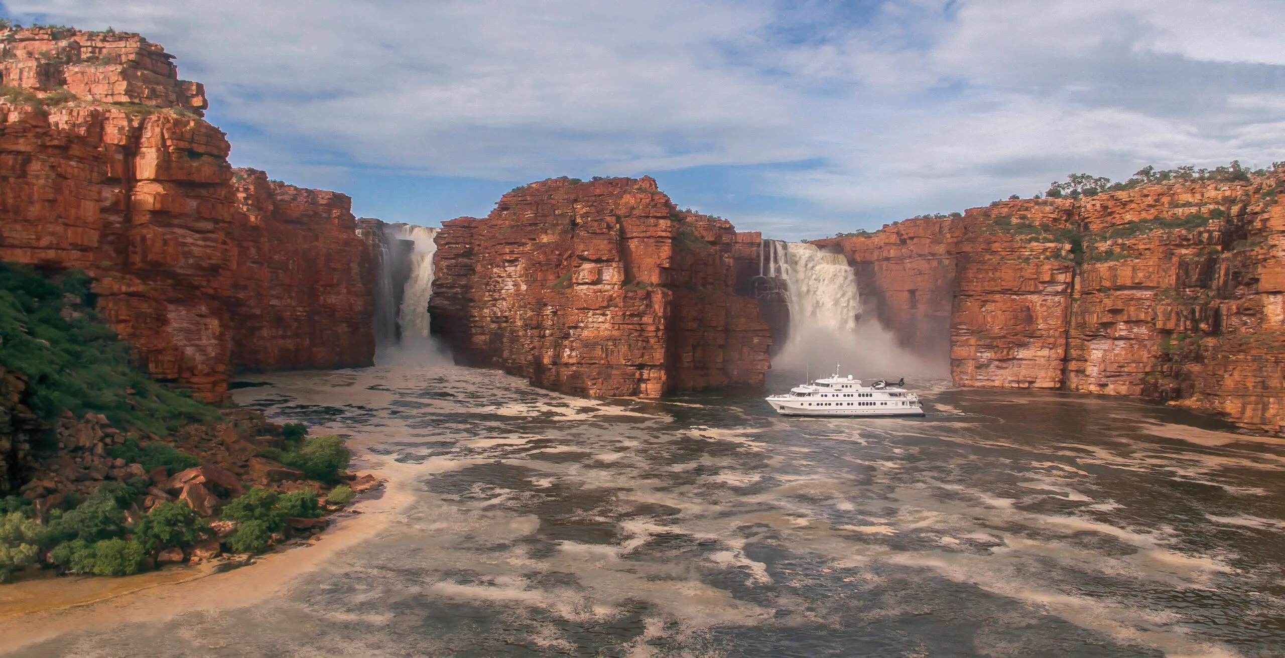 A cruising ship under a waterfall in The Kimberley region of Australia