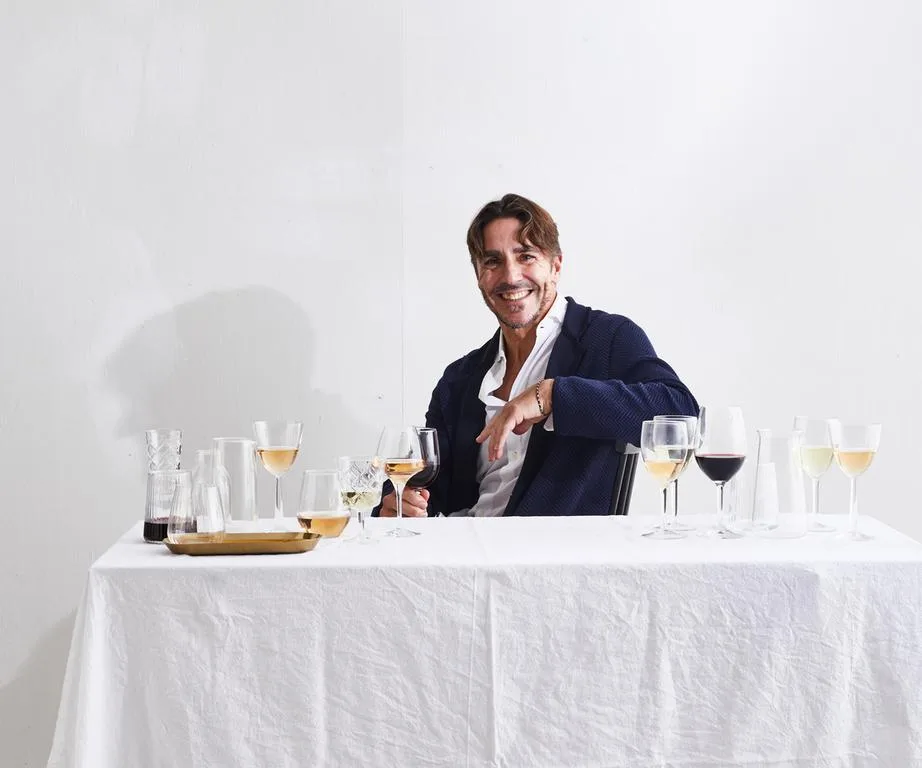 Portrait of Ned Goodwin with glasses of white and red wine on a white tablecloth-covered table