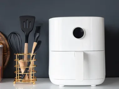 A white air fryer next to kitchen utensils, a cutting board, and a jar of lentils on a countertop.