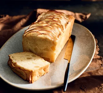 Sliced apple loaf cake on a plate with a gold-handled knife beside it.