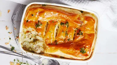 Chicken and leek pie in a white dish with the corner already scooped out