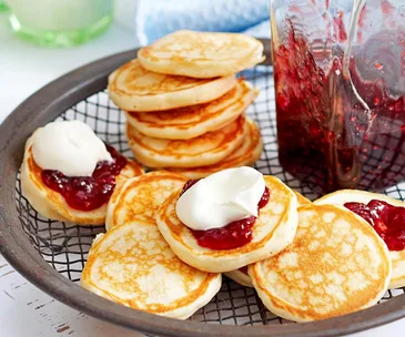 tray of pikelets topped with jam and cream next to jar of jam