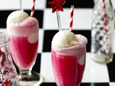 two long soda glasses filled with pink liquid and scoops of vanilla with red and white straws.