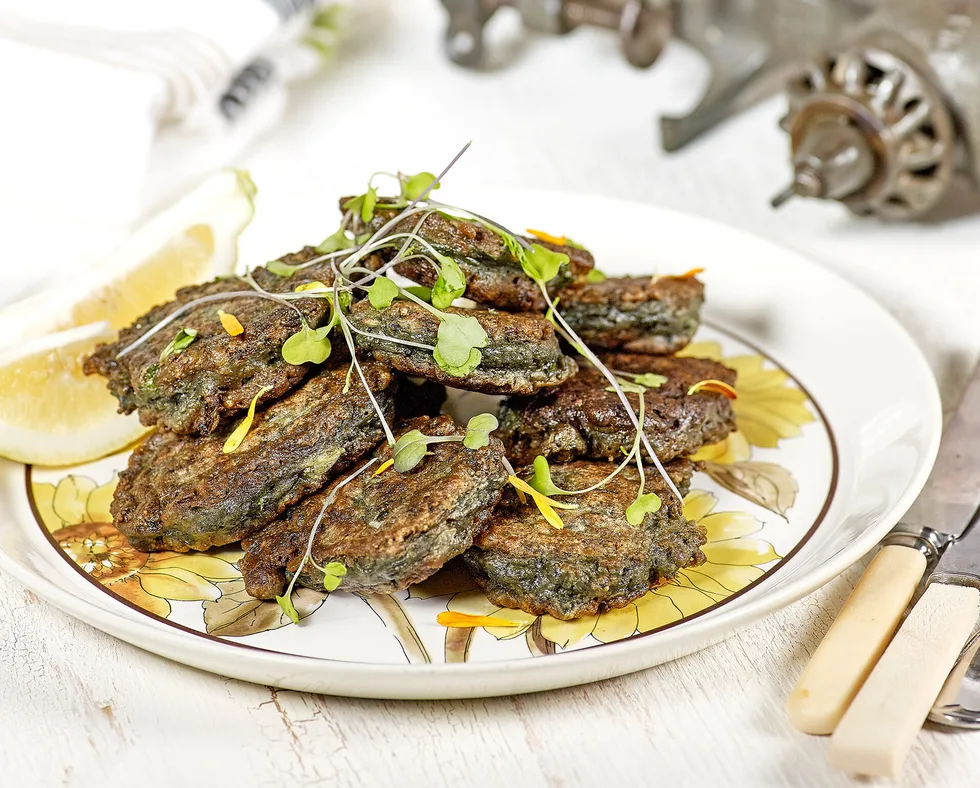 white plate with selection of paua fritters and lemon slices, garnished with fresh herbs