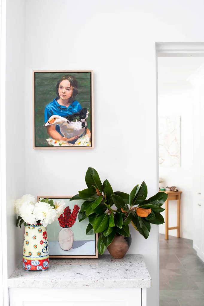 Styled vignette in a home with white interiors featuring a still life painting and a portrait of a girl hung on the wall.