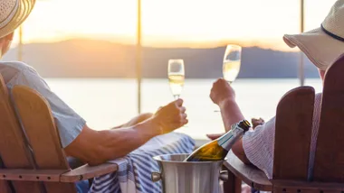 Couple enjoying a wine and looking at the ocean while sitting back on the deck of a cruise ship