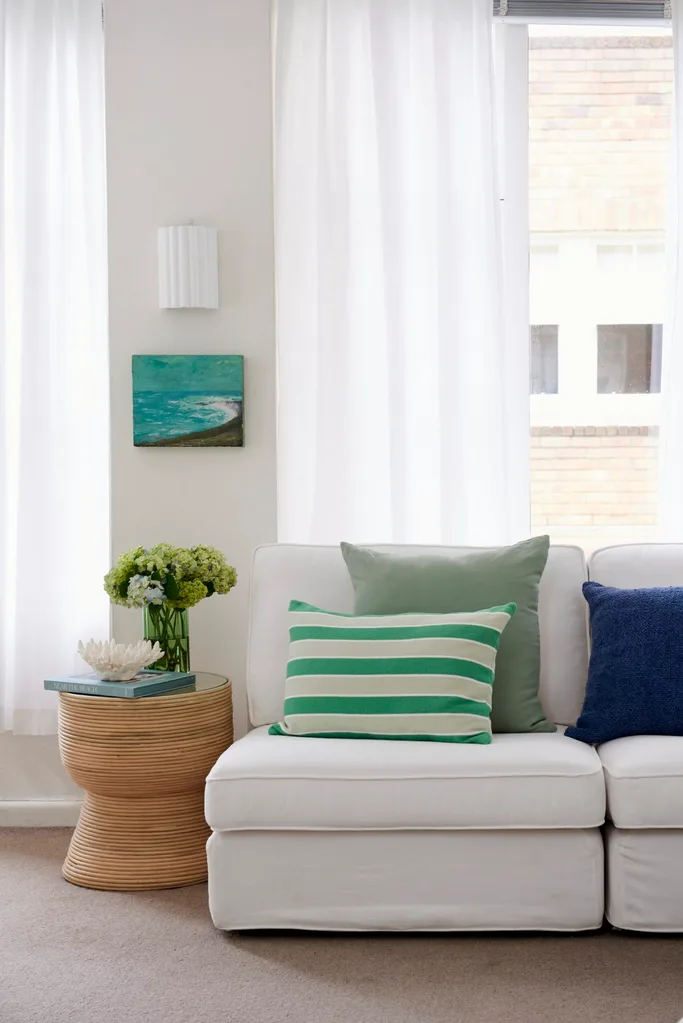 coastal style living room with artwork of beach scene, blue and green pilllows and neutral coloured furniture