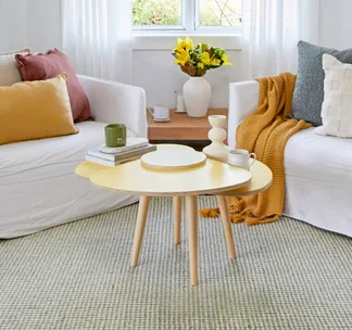 view of coffee table in yellow with white couches behind and mustard, dusty blue and red pillows