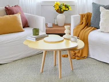 view of coffee table in yellow with white couches behind and mustard, dusty blue and red pillows