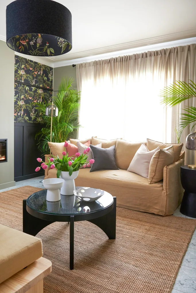 old styling living room decor with black modern coffee table, linen couch and draped curtains. floral wallpaper to the left of the room