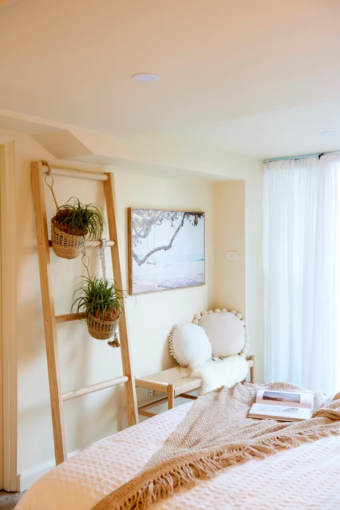 pink bedspread with clay coloured throw facing the wall with ladder and two potted plants