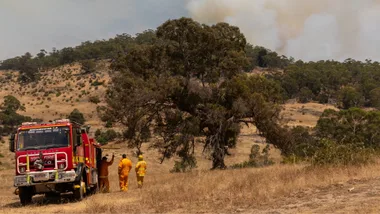 firefighters by a firetrucky with smoke billowing out of hill in harcourt during 2026 january bushfires