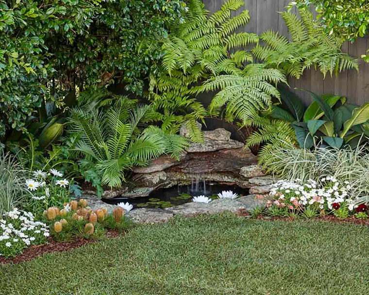 Small backyard pond in a corner of the garden surrounded by flowering plants.