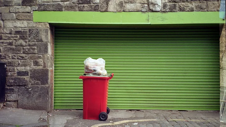 red wheelie bin in front of a green garage door