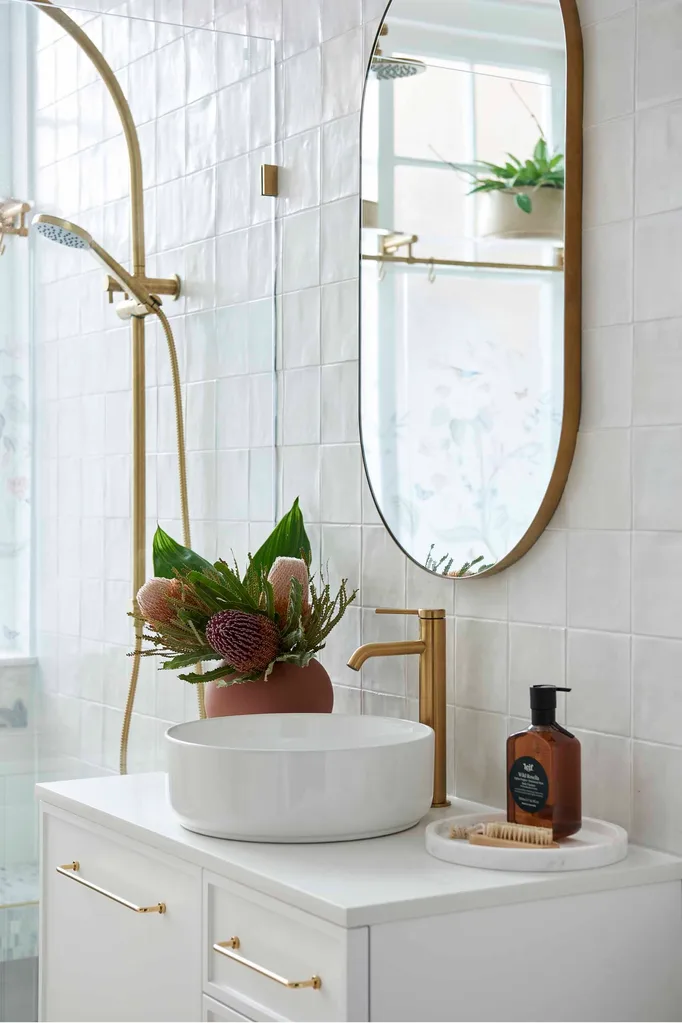 Renovated warm white modern bathroom with white vanity and basin and gold tapware. Bathroom renovation tip for improving house value.
