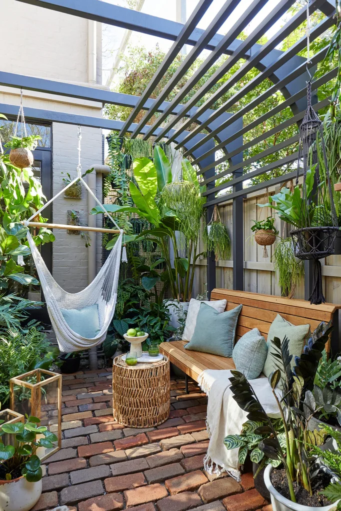 Brick courtyard with a bench seat, overhead pergola and lush greenery