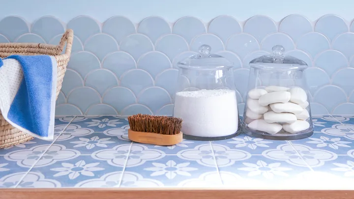 Tiled laundry bench with cleaning products in glass jars next to a wooden scrubbing brush.