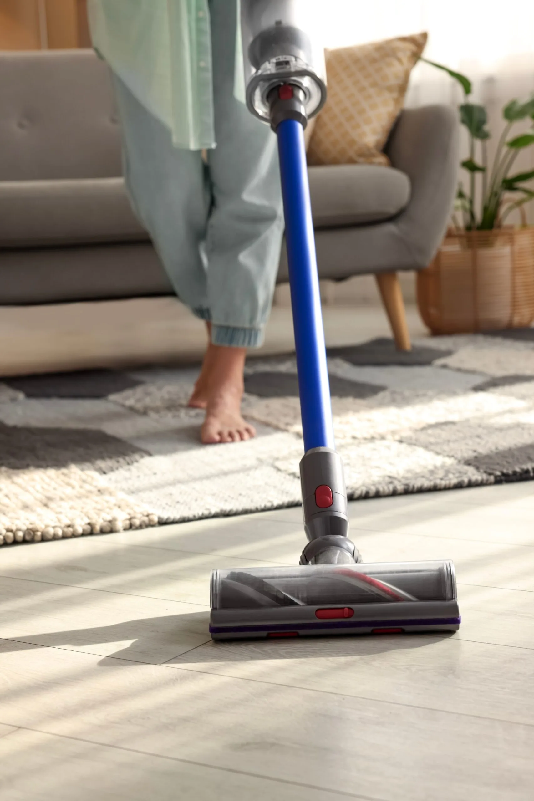 Woman vacuuming floor with cordless vacuum cleaner.