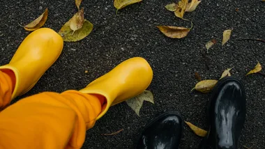 Two people wearing stylish yellow and glossy black gumboots on wet pavement.