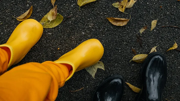 Two people wearing stylish yellow and glossy black gumboots on wet pavement.