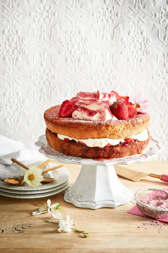 cake stand with sponge cake on it white cream as icing with strawberries piled on top