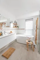 light bright small bathroom design with wooden features like floor mat, towel rack and small side table. big freestanding bath in the middle and vanity with white accents to the left