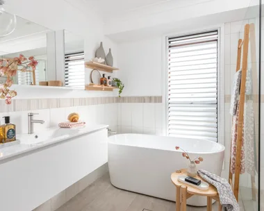 light bright small bathroom design with wooden features like floor mat, towel rack and small side table. big freestanding bath in the middle and vanity with white accents to the left