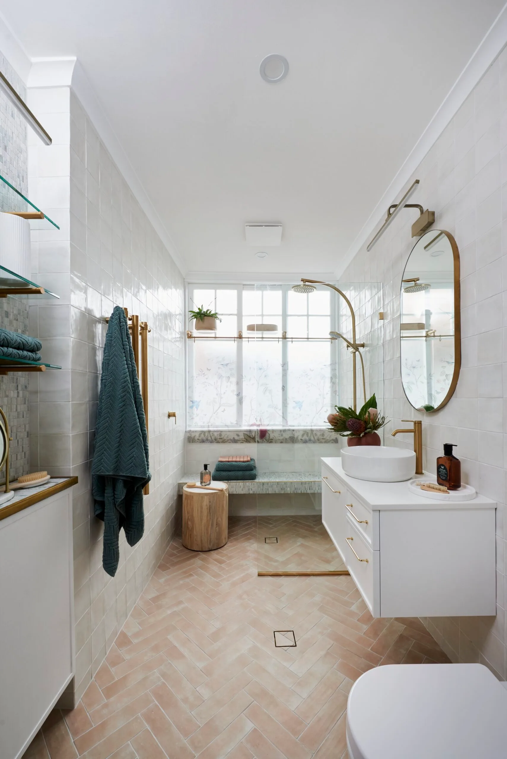 modern small bathroom design with teal towels, copper racks and taps and terracotta herringbone floor tiles