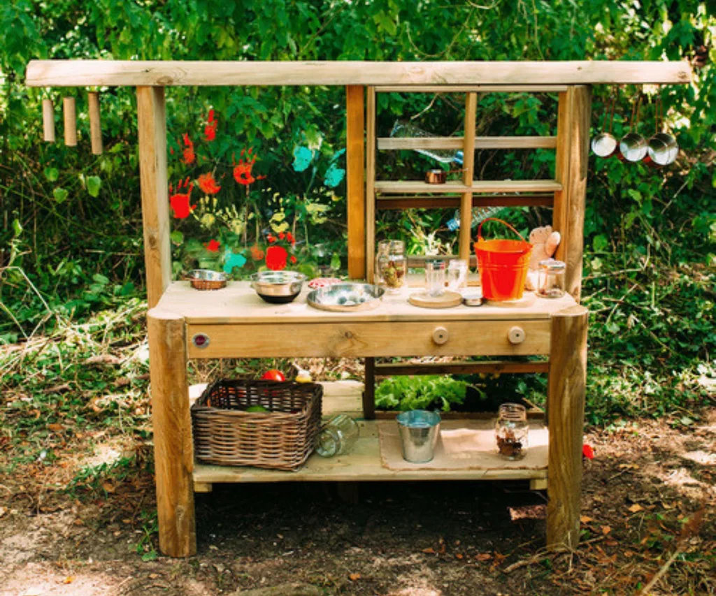 mud pie kids kitchen in grassy area with paint handprints and bucket and other trinkets on top