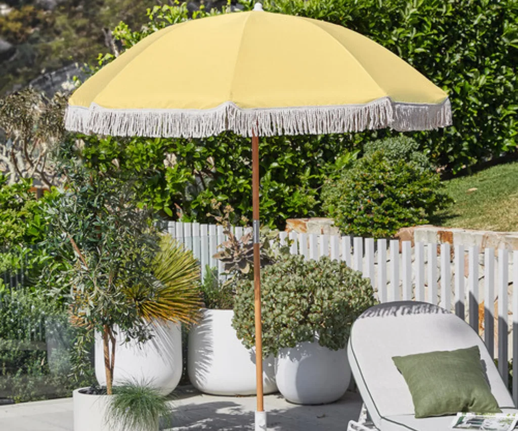 yellow beach umbrella in garden setting with fringe and wooden pole in the middle