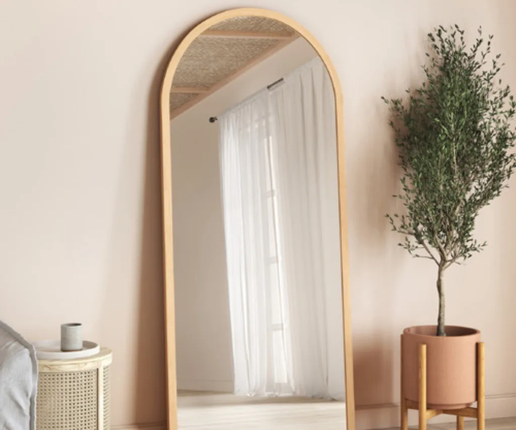 floor length mirror with curved top reflecting flowy white curtain with terracotta pot and olive tree on the side