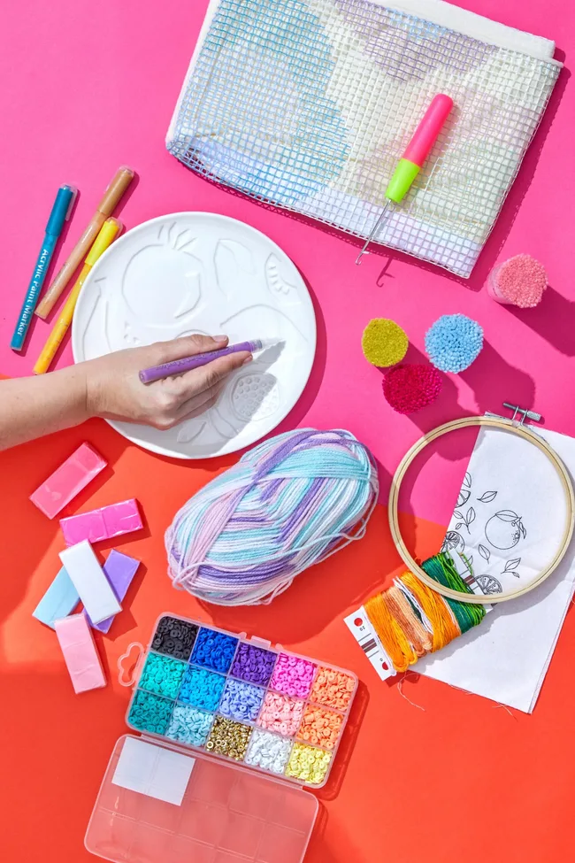 Craft gift ideas including an embroidery hoop, coloured beads, coloured pens and paper on a pink and orange table.