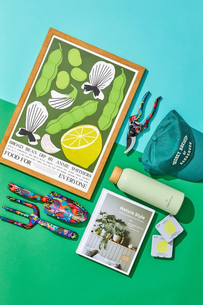 Gifts for gardeners including spades, forks and gardening coffee table books arranged on a blue and green table.