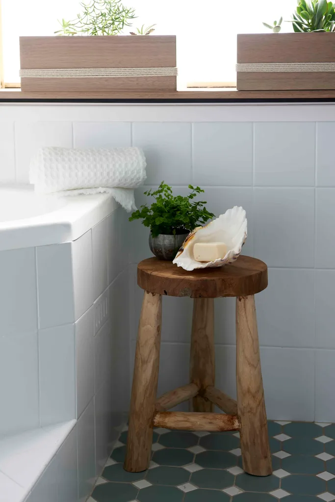 Timber stool in a cosmetically renovated bathroom with white square tiles and blue floor tiles.