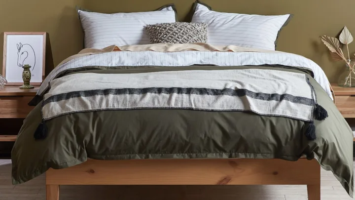 olive and white sheets on a natural wooden bed frame