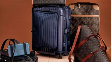 Luxury luggage and bags, including Rimowa and Fendi, displayed against a brown background.