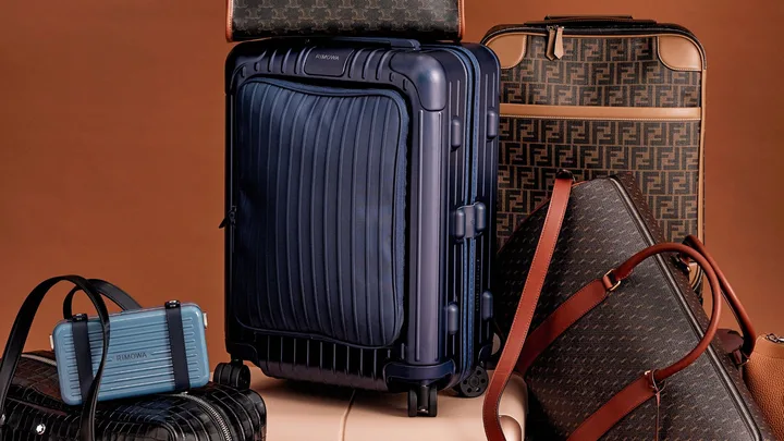 Luxury luggage and bags, including Rimowa and Fendi, displayed against a brown background.