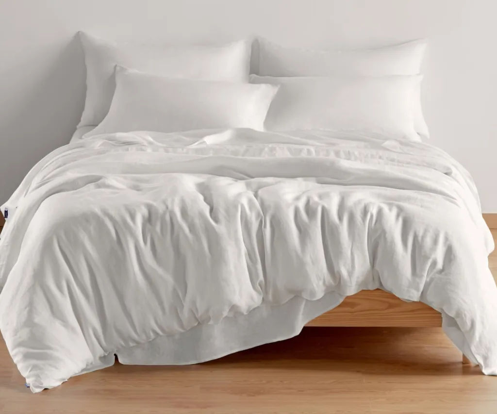 milano sheet set with white duvet hanging over edge of bed onto wooden floors