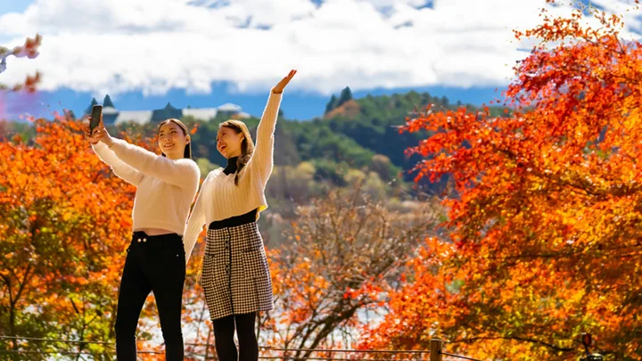 Two people posing for a photo in front of autumn trees.