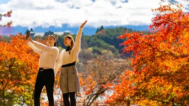 Two people posing for a photo in front of autumn trees.