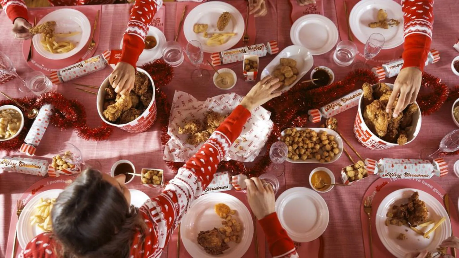 dining table with KFC food laid out and people reaching for food