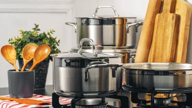 silver cookware sets sitting on a stove surrounded by wooden cutting boards and wooden spoons to share the best cookware sets available